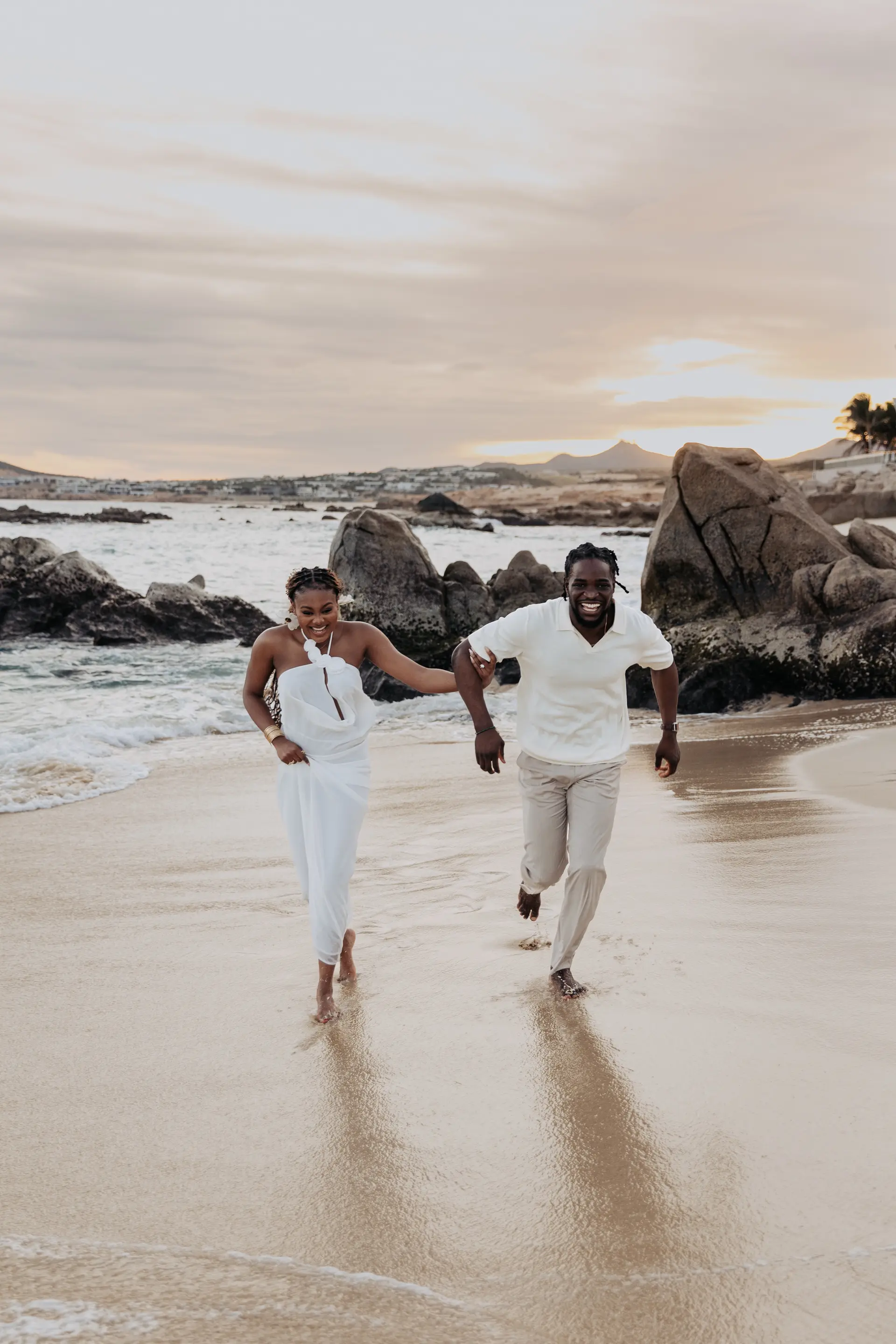 Temiloluwa and Olugbenga running toward the camera on the beach, laughing, black and white