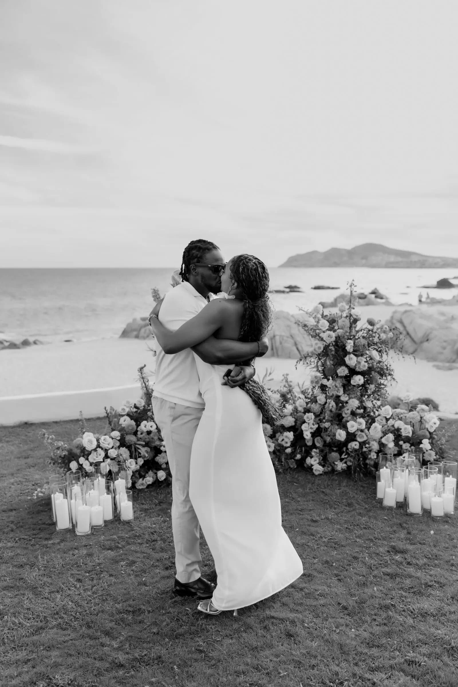 Temi and Olugbenga hugging beside floral columns, black and white